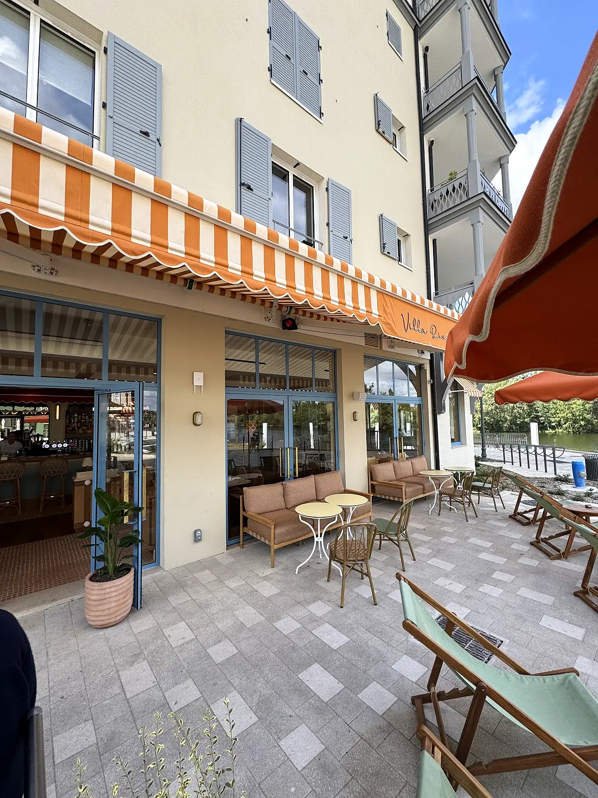 Terrasse élégante avec parasols orange et blanc, mobilier vintage face à bâtisse classique
